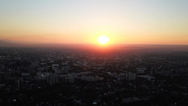 Red sunset over the city of Almaty. Clouds shimmer with different colors from yellow-red to blue. The city is plunged into darkness. Night falls. Lights are on, cars are driving. The view from the top