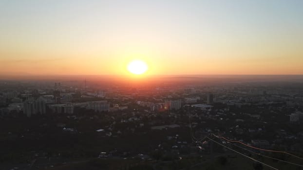 Red sunset over the city of Almaty. Clouds shimmer with different colors from yellow-red to blue. The city is plunged into darkness. Night falls. Lights are on, cars are driving. The view from the top