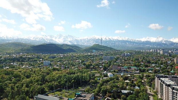 Almaty city Park with rides and a Ferris wheel. Completely green territory, lots of trees, grass, flowers. People are resting. View from a drone. Colored cabs of the Ferris wheel. Clean air and nature