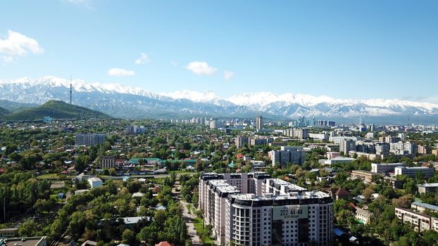 Almaty city Park with rides and a Ferris wheel. Completely green territory, lots of trees, grass, flowers. People are resting. View from a drone. Colored cabs of the Ferris wheel. Clean air and nature