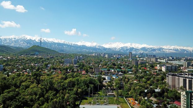 Almaty city Park with rides and a Ferris wheel. Completely green territory, lots of trees, grass, flowers. People are resting. View from a drone. Colored cabs of the Ferris wheel. Clean air and nature