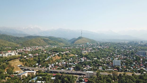 Almaty city Park with rides and a Ferris wheel. Completely green territory, lots of trees, grass, flowers. People are resting. View from a drone. Colored cabs of the Ferris wheel. Clean air and nature