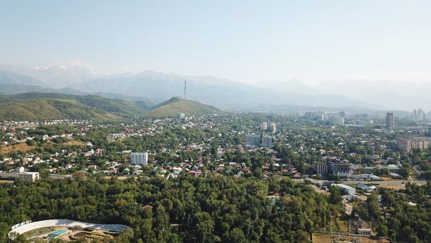 Almaty city Park with rides and a Ferris wheel. Completely green territory, lots of trees, grass, flowers. People are resting. View from a drone. Colored cabs of the Ferris wheel. Clean air and nature