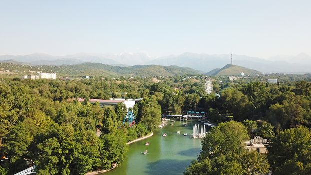 Pond among the green trees of the Park. People relax, go boating, enjoy the fresh air. Family vacation in the Park. The view from the top. In the distance, green hills and the Kok Tobe TV tower.