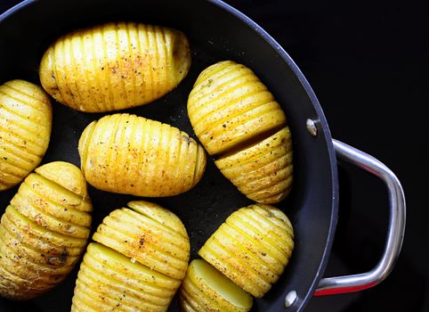 Closeup of sliced baked crispy hasselback potatoes in the pan.