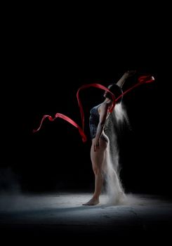 beautiful caucasian woman in a black bodysuit with a sports figure dancing with red ribbon on a black background, explosion and expression in motion
