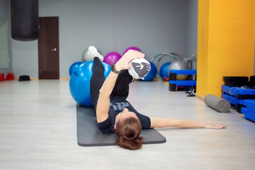 Beautiful young woman performing leg stretching exercises in the gym using a large gymnastic ball