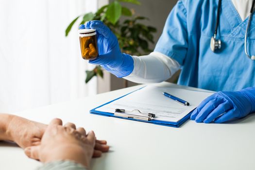 General Practitioner UK GP doctor holding bottle of prescription drugs,handing over to patient during medical check up,healthcare professional prescribing treatment therapy to elderly senior citizen