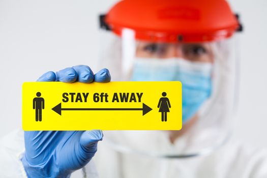 Medical worker in personal protective equipment holding yellow "STAY 6ft AWAY" sign,social physical distancing to prevent and stop spread of viruses and infections,Coronavirus COVID-19 global pandemic