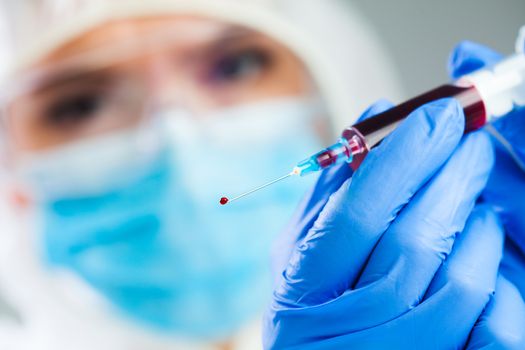 Doctor or lab scientist in personal protective equipment holding syringe full of PRP blood plasma,focus on single drop dripping out of the needle tip,healthcare cure treatment and research for vaccine