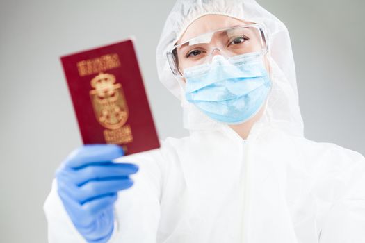 Medical healthcare worker in full personal protective equipment holding red passport,Coronavirus COVID-19 immunity passport/risk free certificate document concept,health passport as proof of recovery