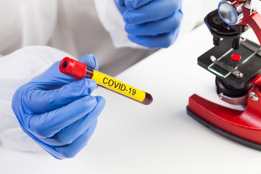 Lab scientist or medical technologist holding a yellow COVID-19 test tube blood sample vacutainer, Coronavirus infected patient specimen ready for microscope laboratory examination check