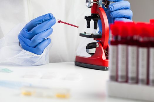 Medical technologist or lab scientist examining Coronavirus patient specimen,placing blood sample under microscope,analysis and research for potential COVID-19 vaccine cure