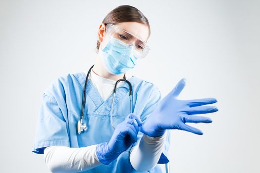 Coronavirus COVID-19 corona virus disease,global world pandemic health crisis,medical healthcare professional female doctor putting on personal protective equipment,adjusting blue gloves and face mask
