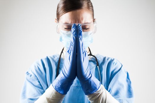 Female doctor praying hands gesture,hope and belief amid worldwide Coronavirus COVID-19 virus disease pandemic crisis outbreak,high global patient death toll and mortality rate with numerous victims