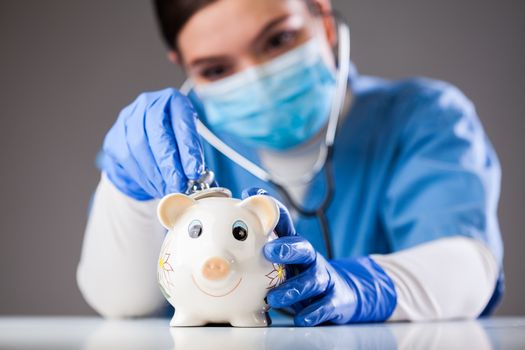 Doctor inspecting piggy bank with stethoscope, economy recession due to global COVID-19 coronavirus world pandemic outbreak,financial hardship & uncertain future,health care,life savings & insurance