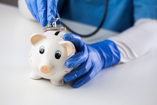 Doctor inspecting piggy bank with stethoscope, economy recession due to global COVID-19 coronavirus world pandemic outbreak,financial hardship & uncertain future,health care,life savings & insurance