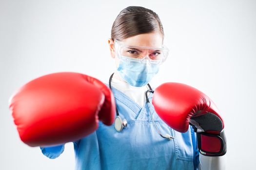 Young female caucasian doctor wearing blue uniform and red boxing gloves, professional and confident, fighting off a disease, immunity and immune system antibodies overcoming viral antigens concept
