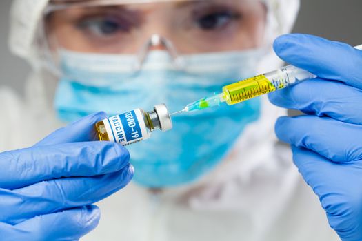 Female medical scientist holding COVID-19 vaccine and syringe jab with yellow liquid,groundbreaking cure for Coronavirus disease,vial ampoule remedy for treating acute respiratory pneumonia patients