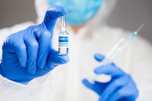 Medical laboratory scientist technician holding a syringe and COVID-19 coronavirus disease vaccine ampoule, illustration of a deadly virus cure, global worldwide SARS-CoV-2 pandemic crisis outbreak