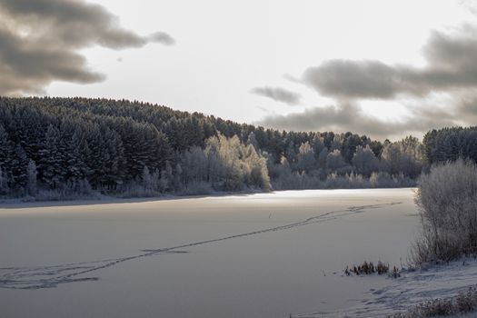 Dramatic sky with clouds over the winter forest and lake. Winter and frosty nature. Frozen lake near the forest, all covered in snow.