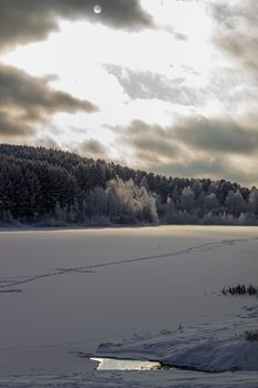 Dramatic sky with clouds over the winter forest and lake. Winter and frosty nature. Frozen lake near the forest, all covered in snow.