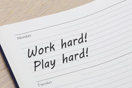 A Work hard play hard reminder note in a diary page