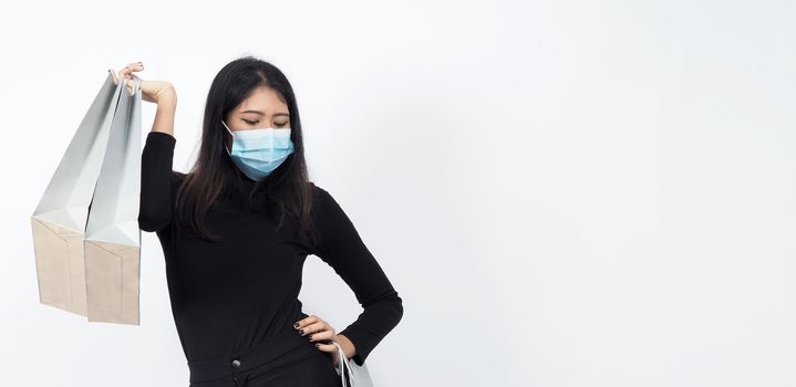 Asian woman holding shopping bags in her hand and wearing medical face mask to protect coronavirus or Covid 19 that is pandemic virus which represent shopper in new normal situatiuon and shop lover.