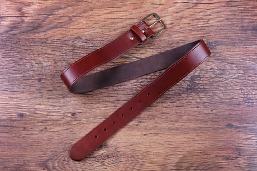 A brown leather belt on a wood background