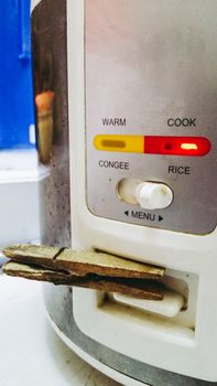 Damaged rice cooker, supported by a clothes hook so it can work, concept or humor image