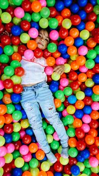 little smiling girl playing lying in colorful balls park playground