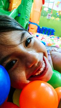 little smiling girl playing lying in colorful balls park playground