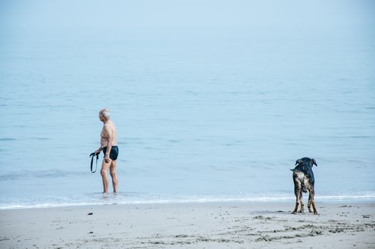 Elderly man with his dog on the beach enjoying summer
