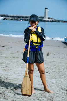 Young woman paddler smiling with an oar in hand at the seashore