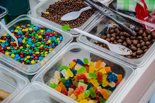 A sample of several candies in plastic containers: gummies, colored candies, chocolates, etc.