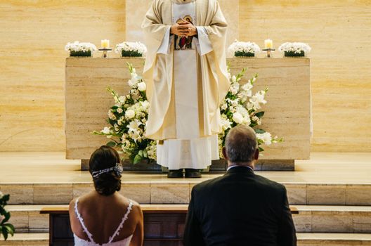 Newlyweds sitting in front of the Bride and groom sitting in front of the altar during the wedding ceremonyaltar during the wedding ceremony