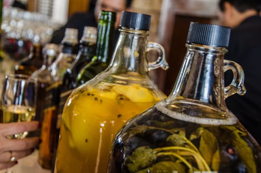 Two large glass bottles of pisco with macerated fruit with the background of a bar