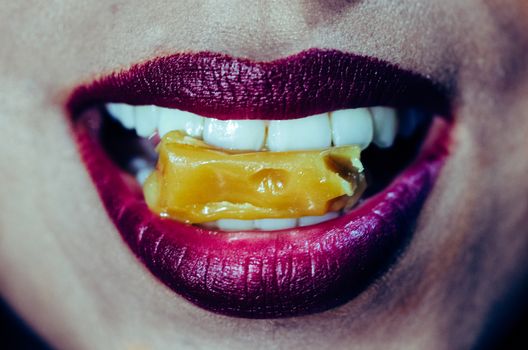 Close-up of woman mouth biting caramel candy with purple lips