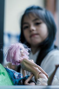 Cute little girl playing with toy doll, doll close-up with defocused girl background, concept image