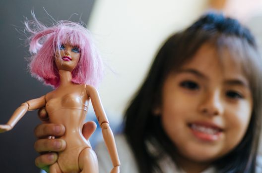 Cute little girl playing with toy doll, doll close-up with defocused girl background, concept image