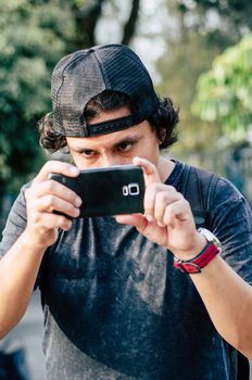 Portrait of an attractive teen boy holding his smartphone with his hand and take photograph. Use the technology of outdoor smartphones to take pictures.