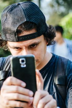 Portrait of an attractive teen boy holding his smartphone with his hand and take photograph. Use the technology of outdoor smartphones to take pictures.