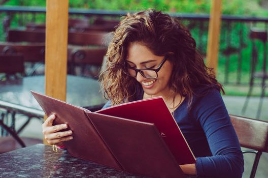 A smiling woman in a restaurant with the menu in hands, woman with glasses, intellectual woman