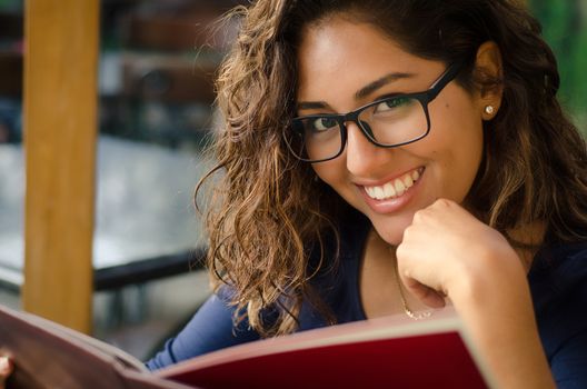 A smiling woman in a restaurant with the menu in hands, woman with glasses, intellectual woman