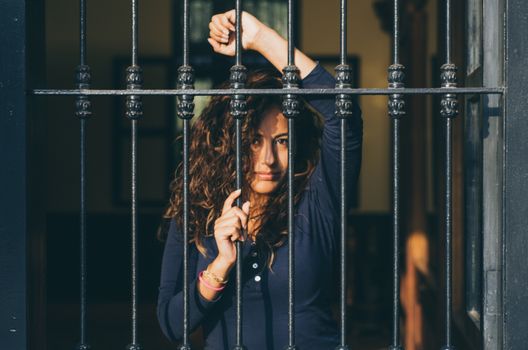 Young girl closed behind bars, network, as in prison. looking sexy with serious and smiling look