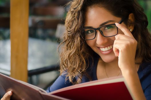 A smiling woman in a restaurant with the menu in hands, woman with glasses, intellectual woman