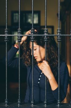 Young girl closed behind bars, network, as in prison. looking sexy with serious and smiling look