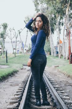 Young sexy girl with long hair in jeans on a railway. Alluring woman looking at camera and smiling