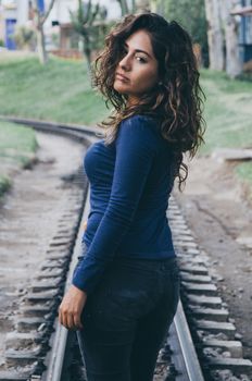 Young sexy girl with long hair in jeans on a railway. Alluring woman looking at camera and smiling