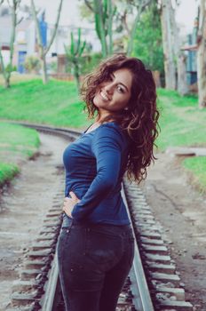 Young sexy girl with long hair in jeans on a railway. Alluring woman looking at camera and smiling